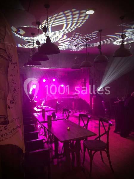 Salle de restaurant avec éclairage tamisé et projecteurs roses créant une ambiance festive.