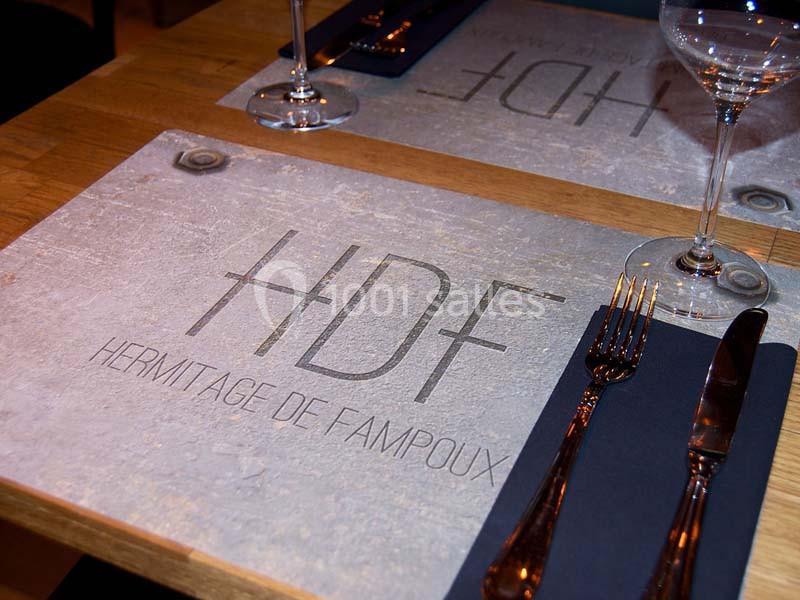 Set de table avec le logo ’Hermitage de Fampoux’ gravé, accompagné de couverts et d'un verre sur une table en bois.