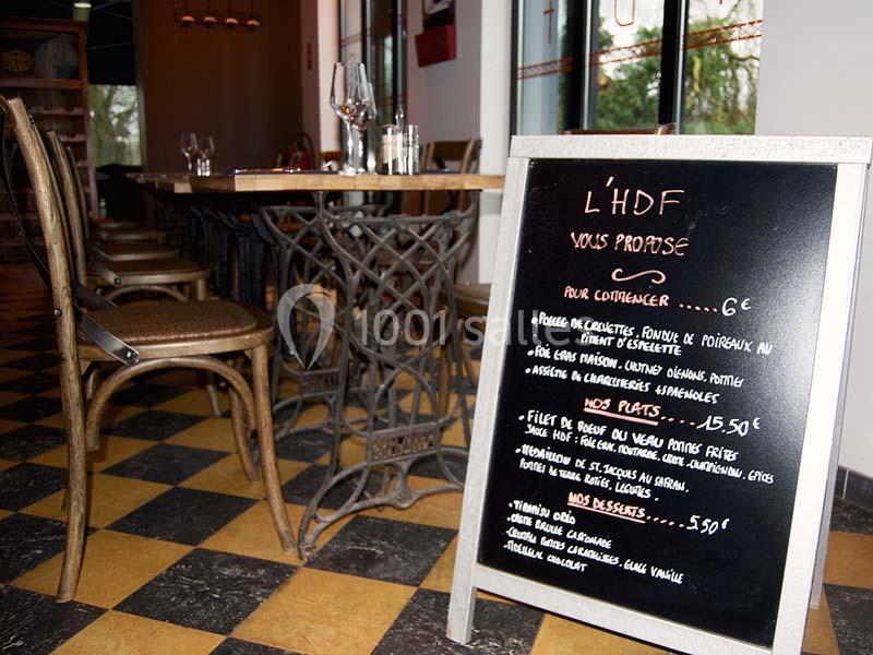 Ardoise de menu écrite à la craie devant des tables et chaises dans un restaurant au sol en damier.