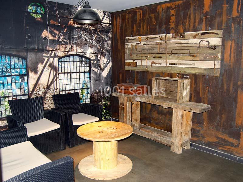 Espace intérieur décoré de meubles rustiques, avec un mur d’outils anciens et un coin salon en fauteuils noirs.