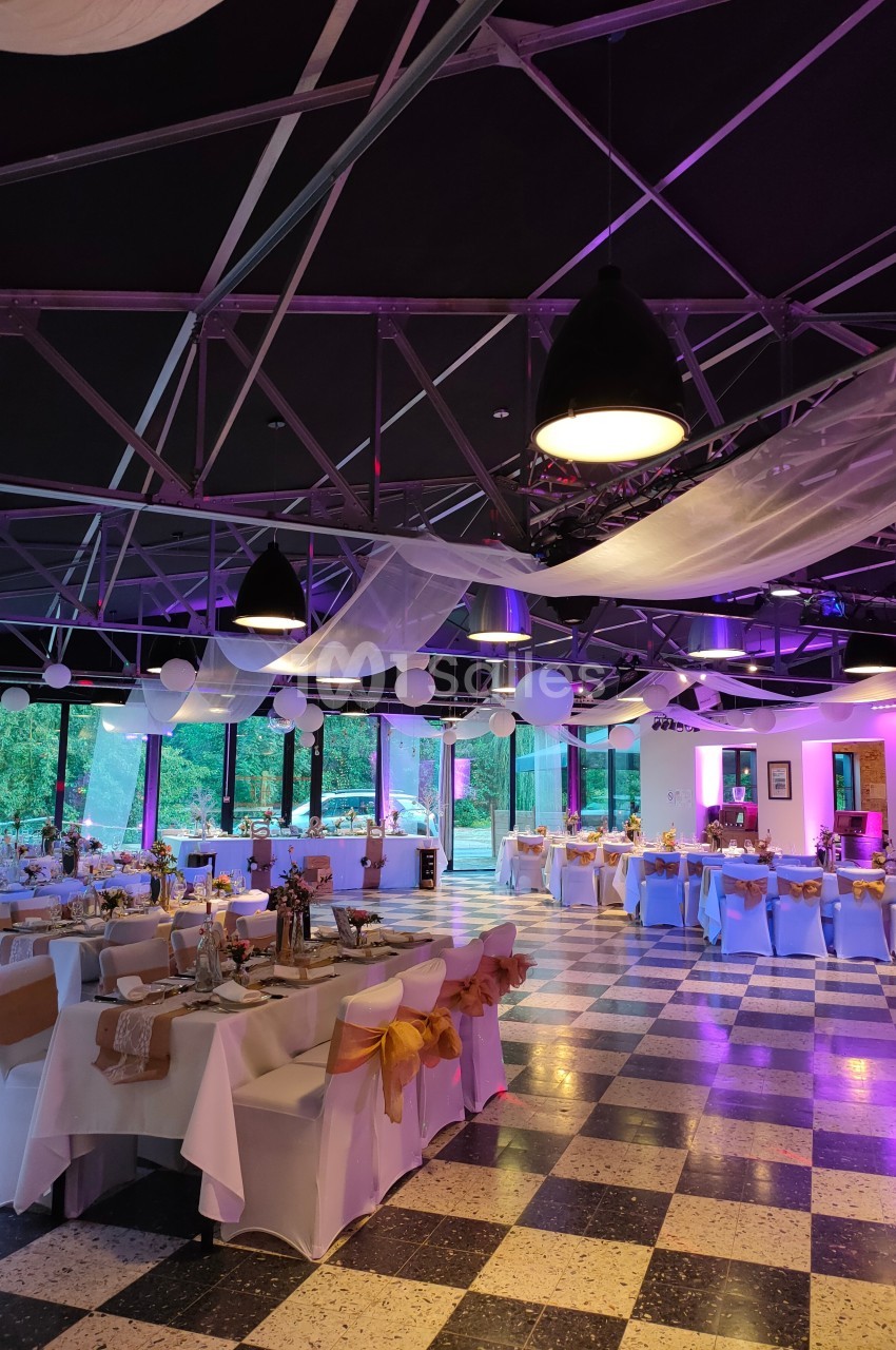 Salle de réception décorée avec des tables dressées, des guirlandes lumineuses et une ambiance lumineuse violette.
