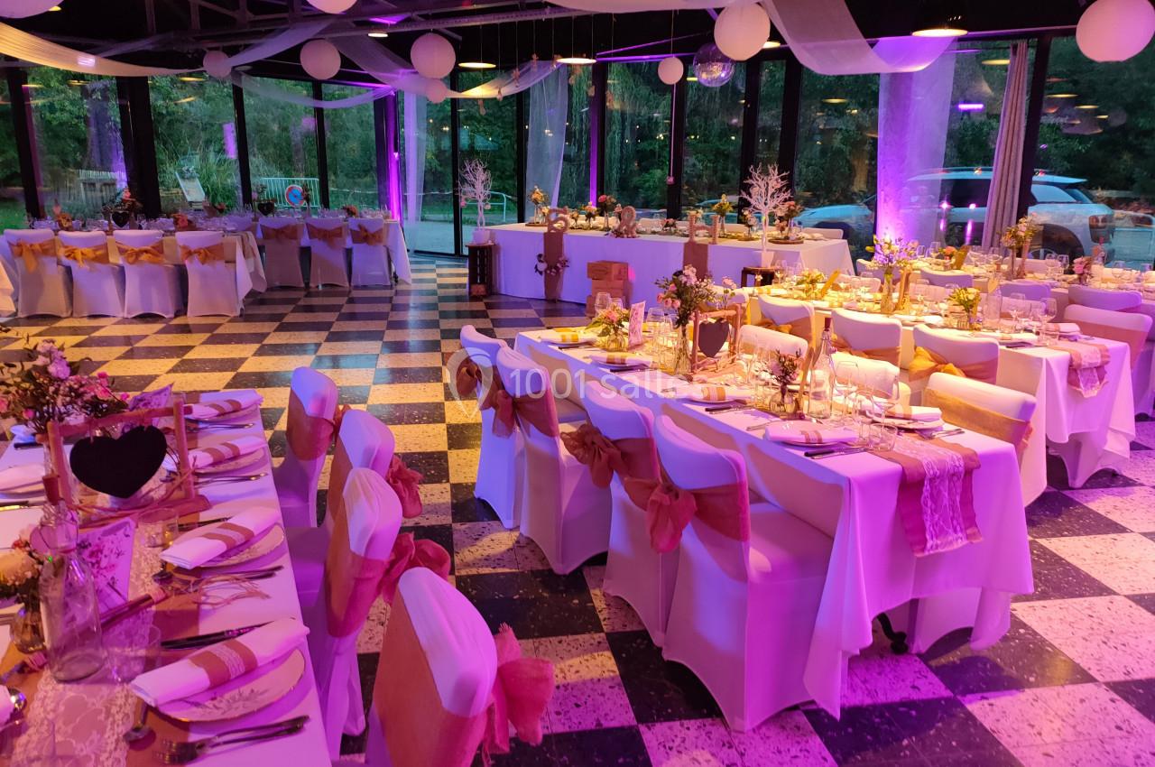 Salle de réception décorée pour un événement, avec tables dressées, chaises ornées de rubans et éclairage rose.