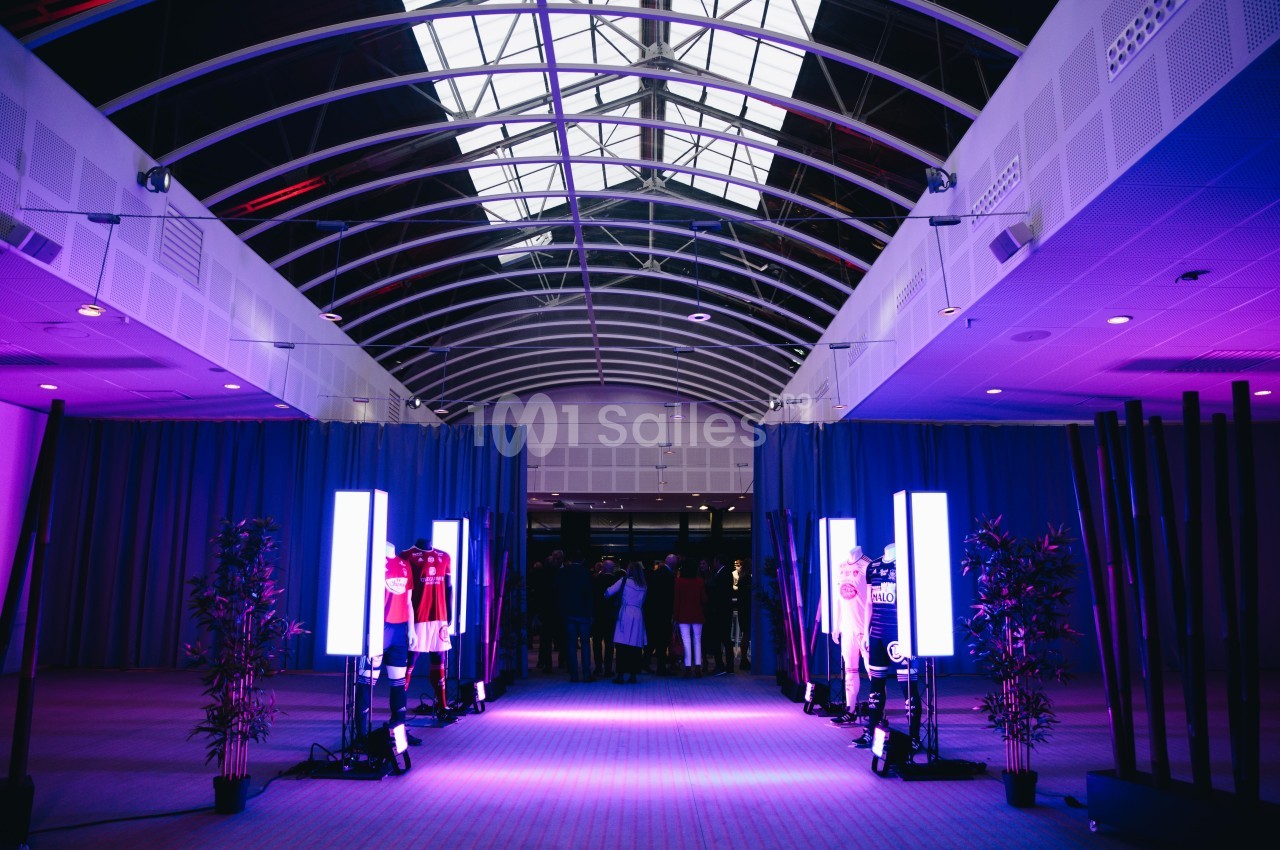 Vue d'un hall avec un plafond en verrière, éclairé par des lumières violettes, et des mannequins exposant des vêtements.
