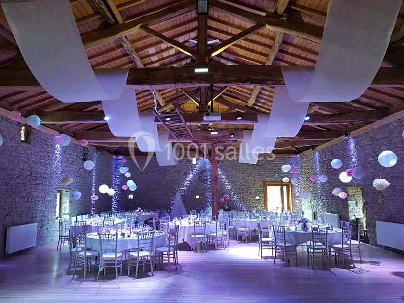 Salle de réception en pierre avec poutres apparentes, tables rondes décorées et éclairage tamisé.