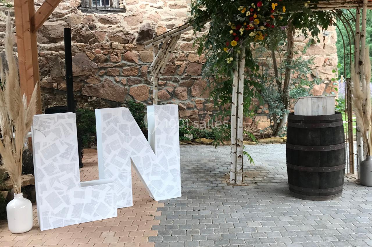 Structure en bois avec décorations de mariage, incluant des lettres blanches, un tonneau et des fleurs suspendues.