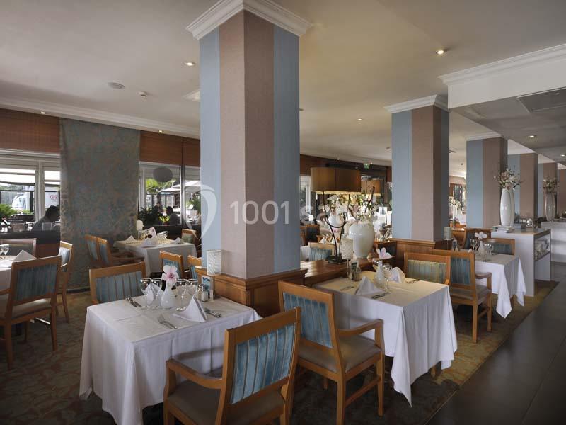 Salle de restaurant élégante avec des tables dressées, nappes blanches, chaises en bois et décorations florales.