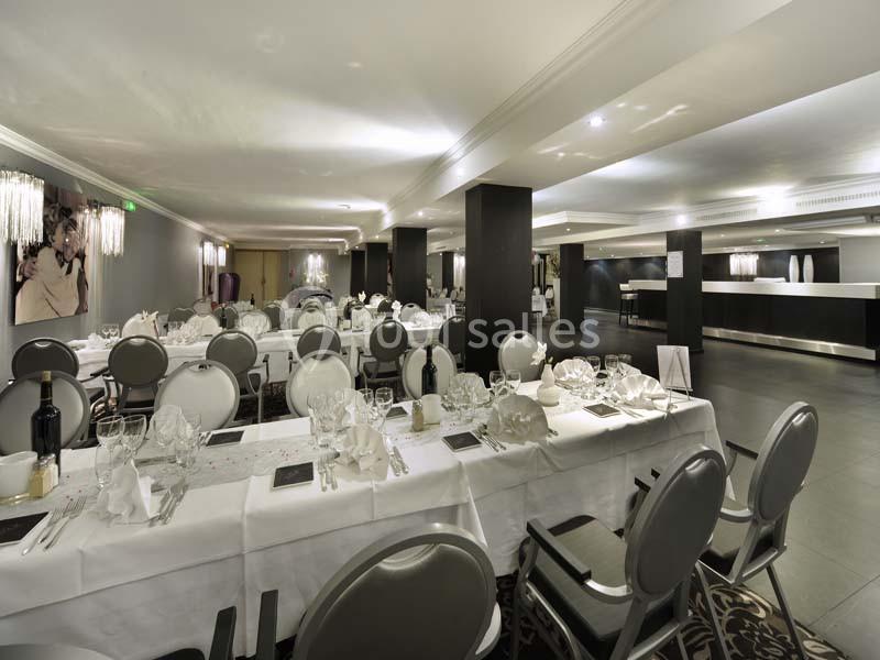 Salle de réception élégante avec des tables dressées, nappes blanches, chaises grises et éclairage moderne.
