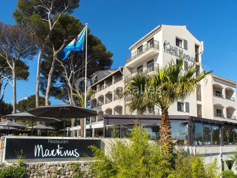 Façade d'un hôtel entouré de palmiers et de pins, avec une enseigne indiquant ’Restaurant Martinus’.