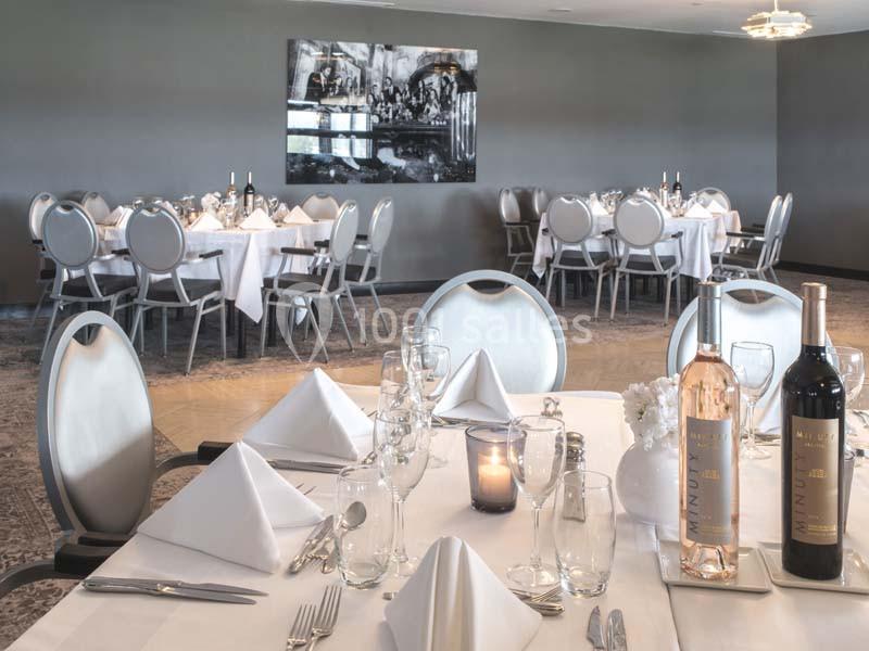 Salle de restaurant élégante avec tables dressées, nappes blanches, bouteilles de vin et décoration moderne.