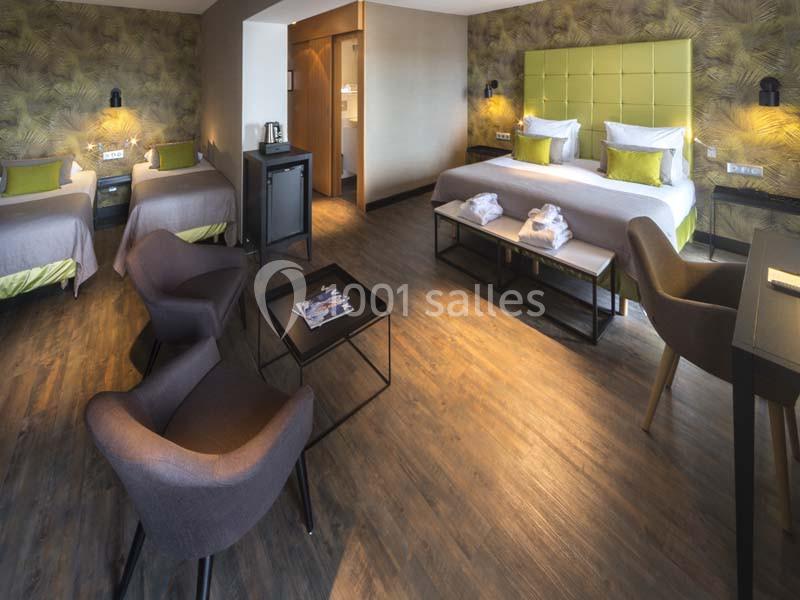 Chambre d'hôtel spacieuse avec lit double, deux lits simples, coin salon, parquet et décoration moderne.