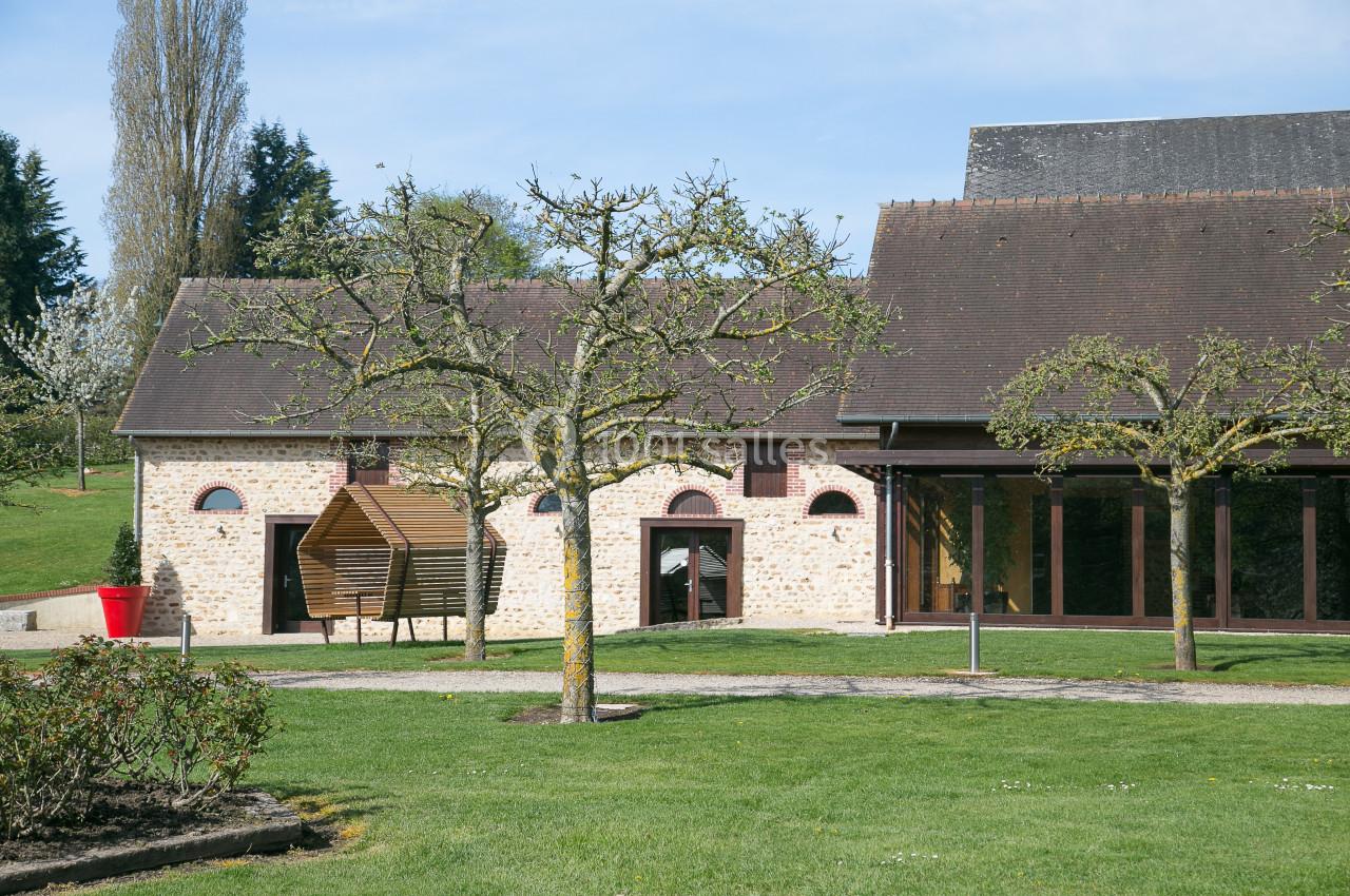 Bâtiment en pierre avec toit en ardoise, entouré d'arbres et d'une pelouse bien entretenue sous un ciel dégagé.
