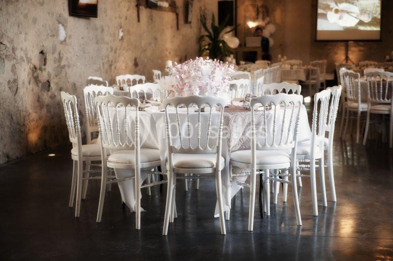 Salle décorée avec des tables rondes, nappes blanches, chaises élégantes et centre de table floral rose.