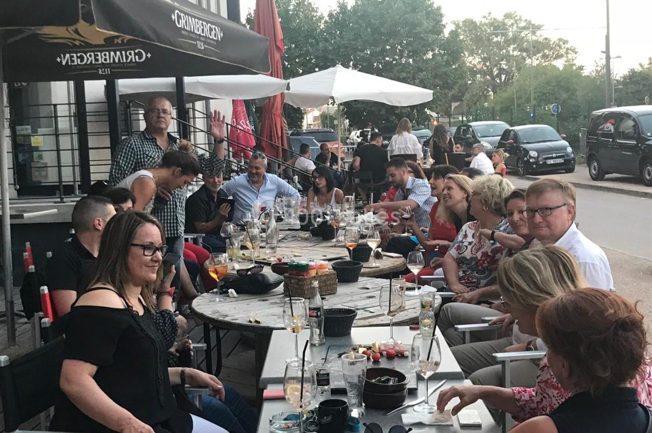 Groupe de personnes assises autour de tables en terrasse, partageant un moment convivial avec des boissons et des plats.
