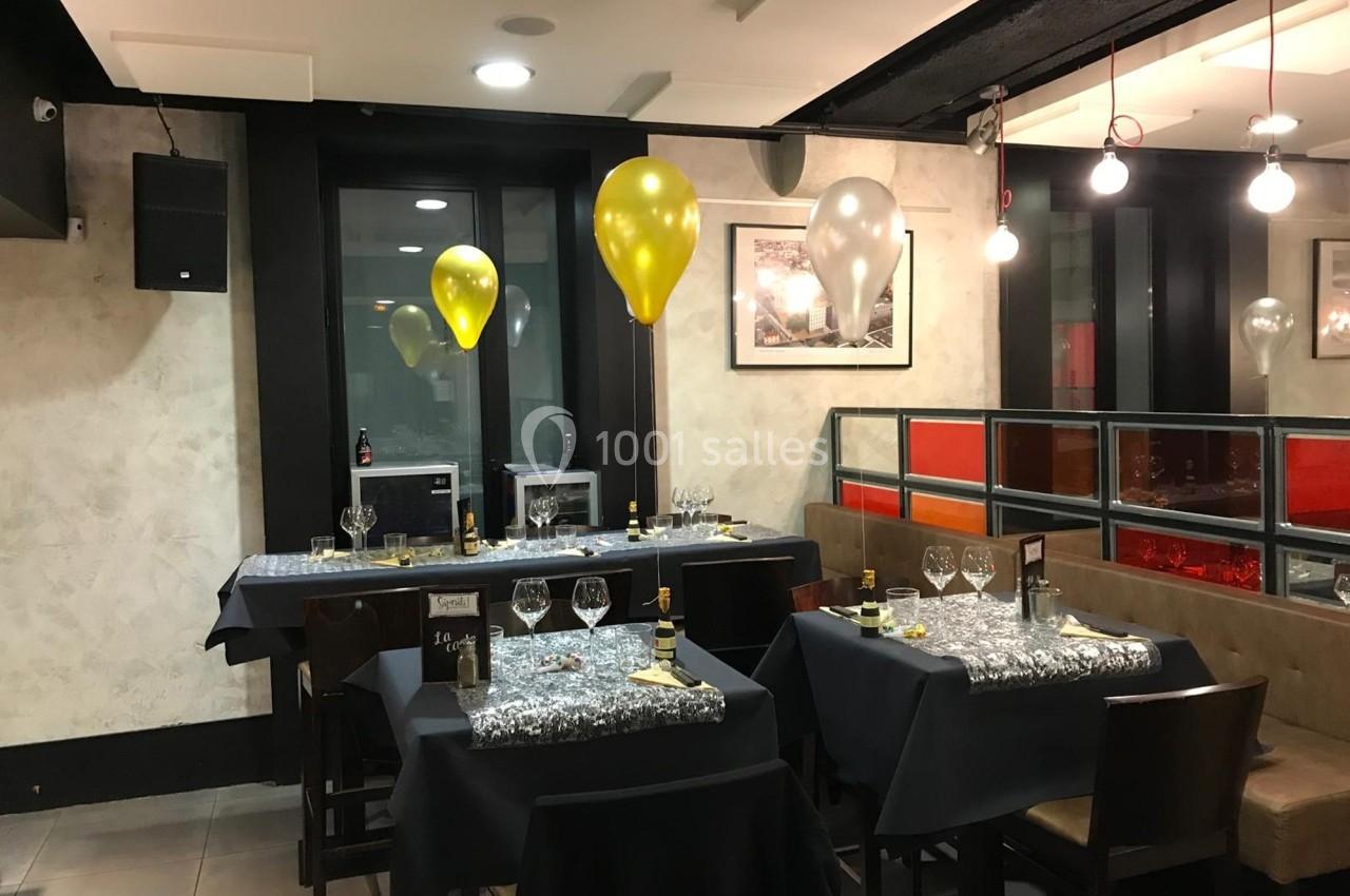 Salle de restaurant décorée avec des ballons dorés et argentés, tables dressées avec nappes noires et chemins de table…