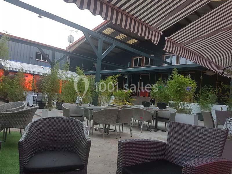 Terrasse extérieure avec mobilier en rotin, tables et chaises sous des stores rayés, entourée de plantes et bambous.