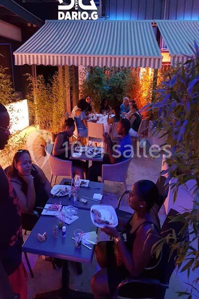 Personnes dînant en terrasse le soir, entourées de bambous et éclairées par une lumière tamisée.