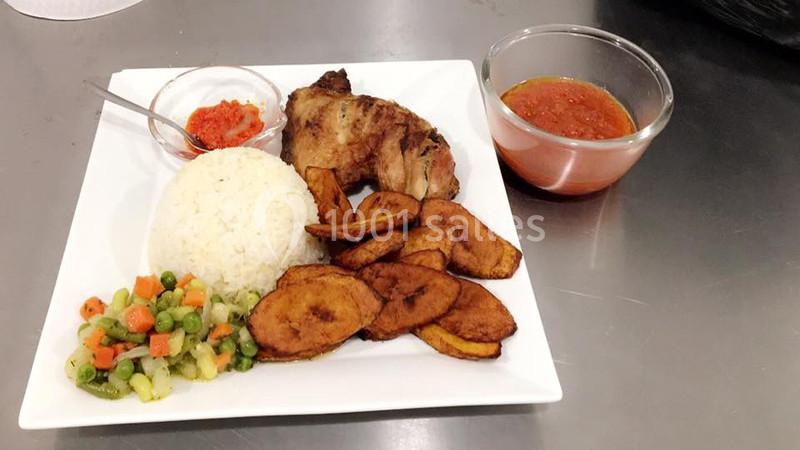 Assiette contenant du riz, du poulet grillé, des bananes plantains frites, des légumes sautés et des sauces en…