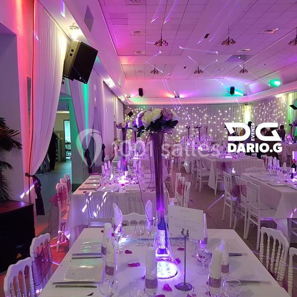 Salle de réception décorée avec des tables dressées, éclairage coloré et centre de table floral.