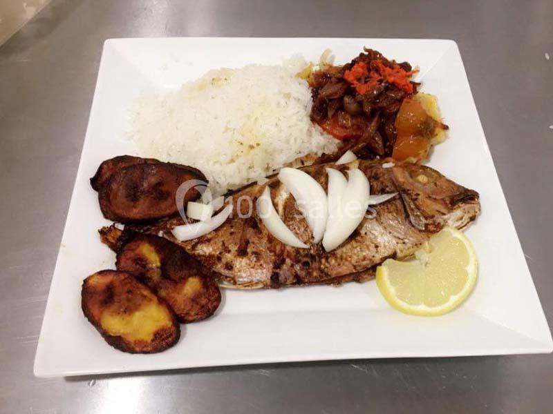 Assiette contenant du poisson grillé garni d'oignons, riz blanc, bananes plantains frites et légumes sautés.