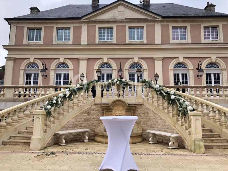 Façade d'un bâtiment élégant avec escalier en pierre décoré de fleurs, table haute blanche au premier plan.