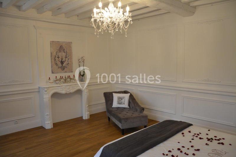 Chambre élégante avec moulures blanches, cheminée décorative, lustre en cristal et pétales de rose sur le lit.