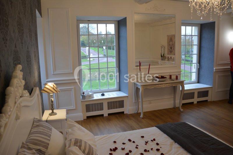Chambre lumineuse avec lit décoré de pétales de rose, fenêtres donnant sur un jardin et mobilier blanc élégant.