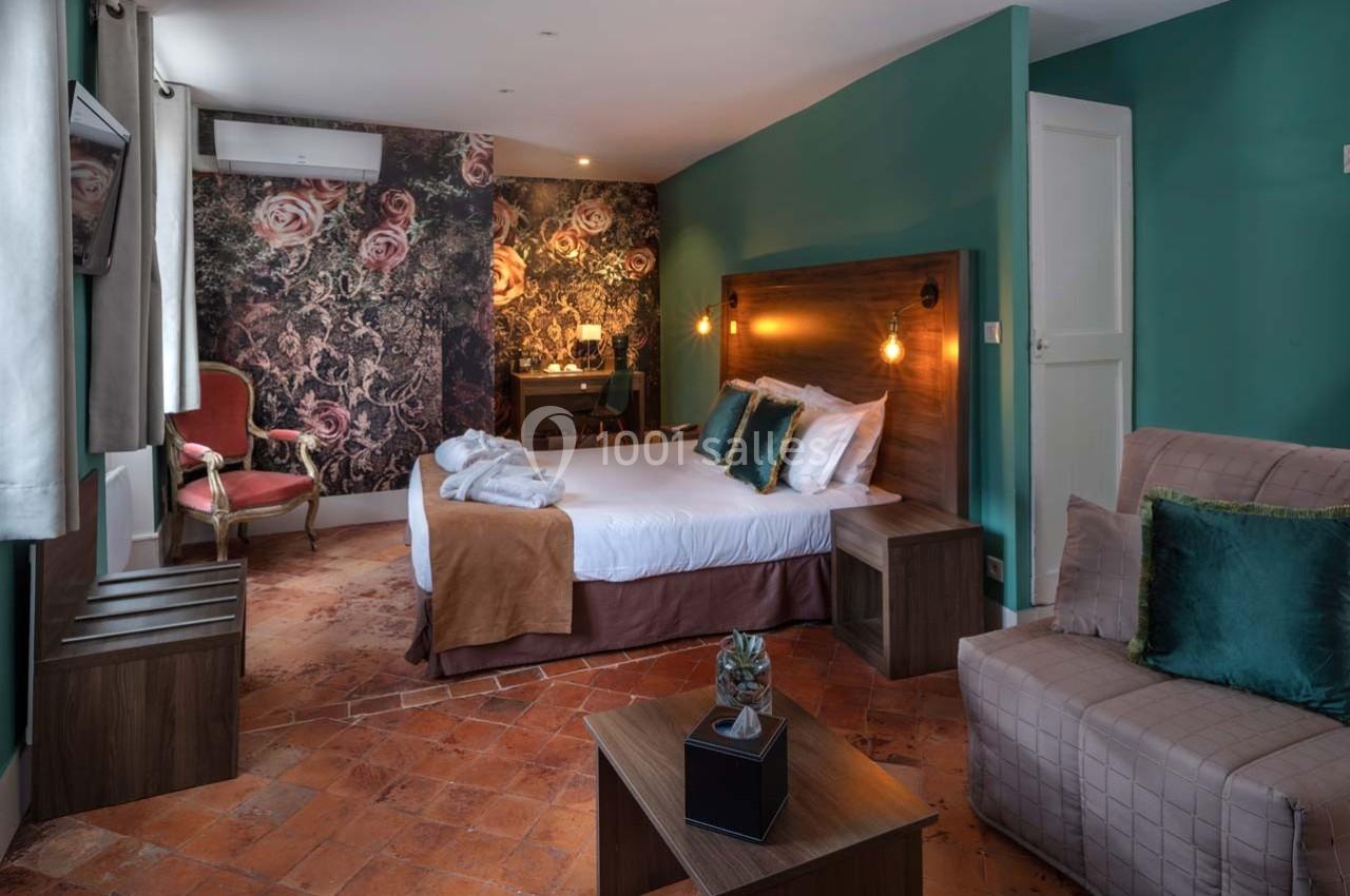 Chambre lumineuse avec lit double, fauteuils, bureau, murs décorés de motifs floraux et sol en carreaux de terre cuite.