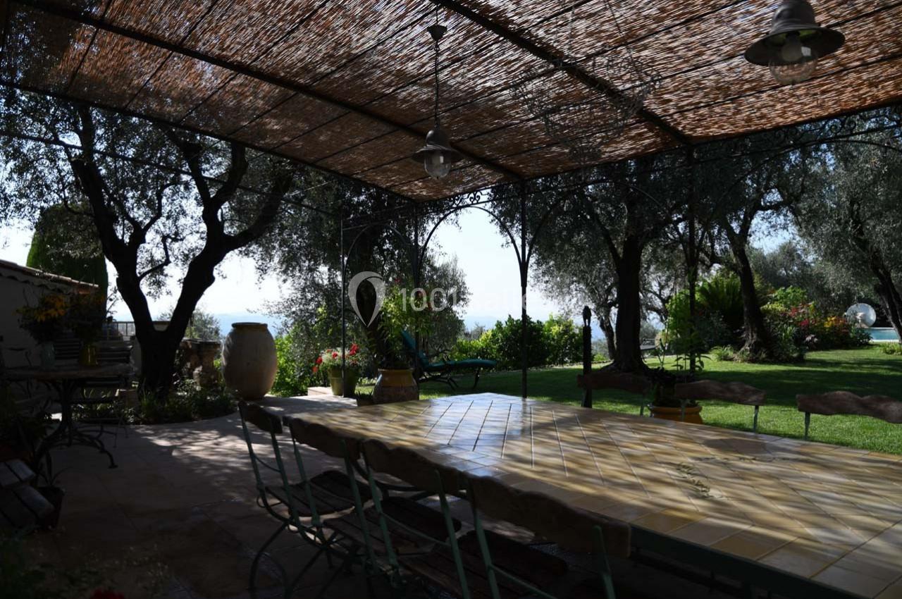 Terrasse ombragée avec une grande table en céramique, entourée d'oliviers et donnant sur un jardin verdoyant.