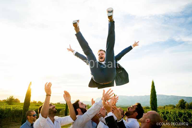 Un groupe d'hommes en costume lance un autre homme en l'air lors d'une célébration en extérieur.