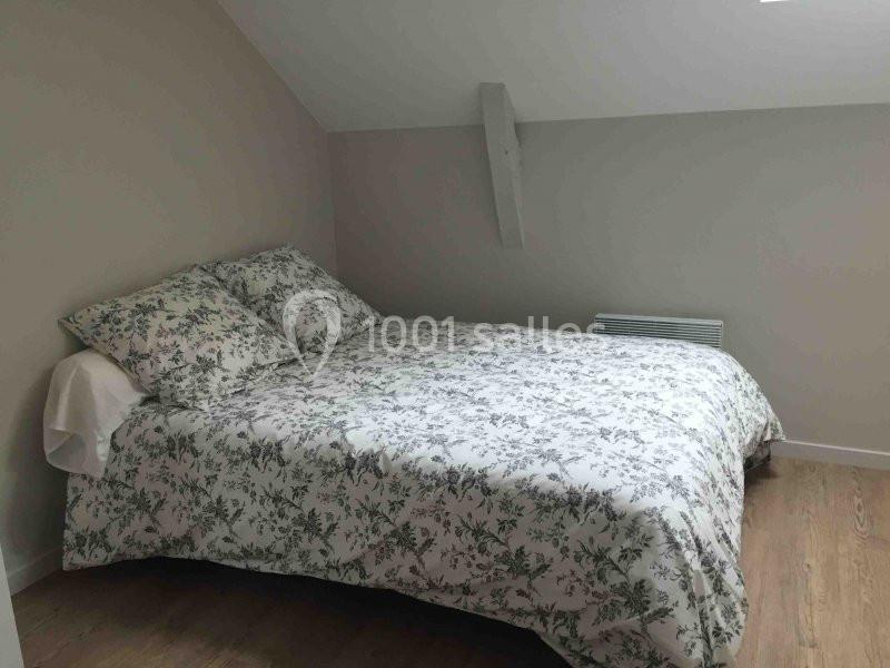Lit double avec une housse de couette à motif floral dans une chambre mansardée aux murs clairs et au sol en bois.