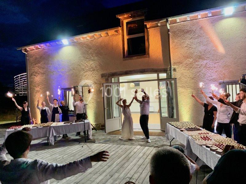 Des personnes dansent avec des cierges magiques allumés sur une terrasse en bois devant une maison éclairée.