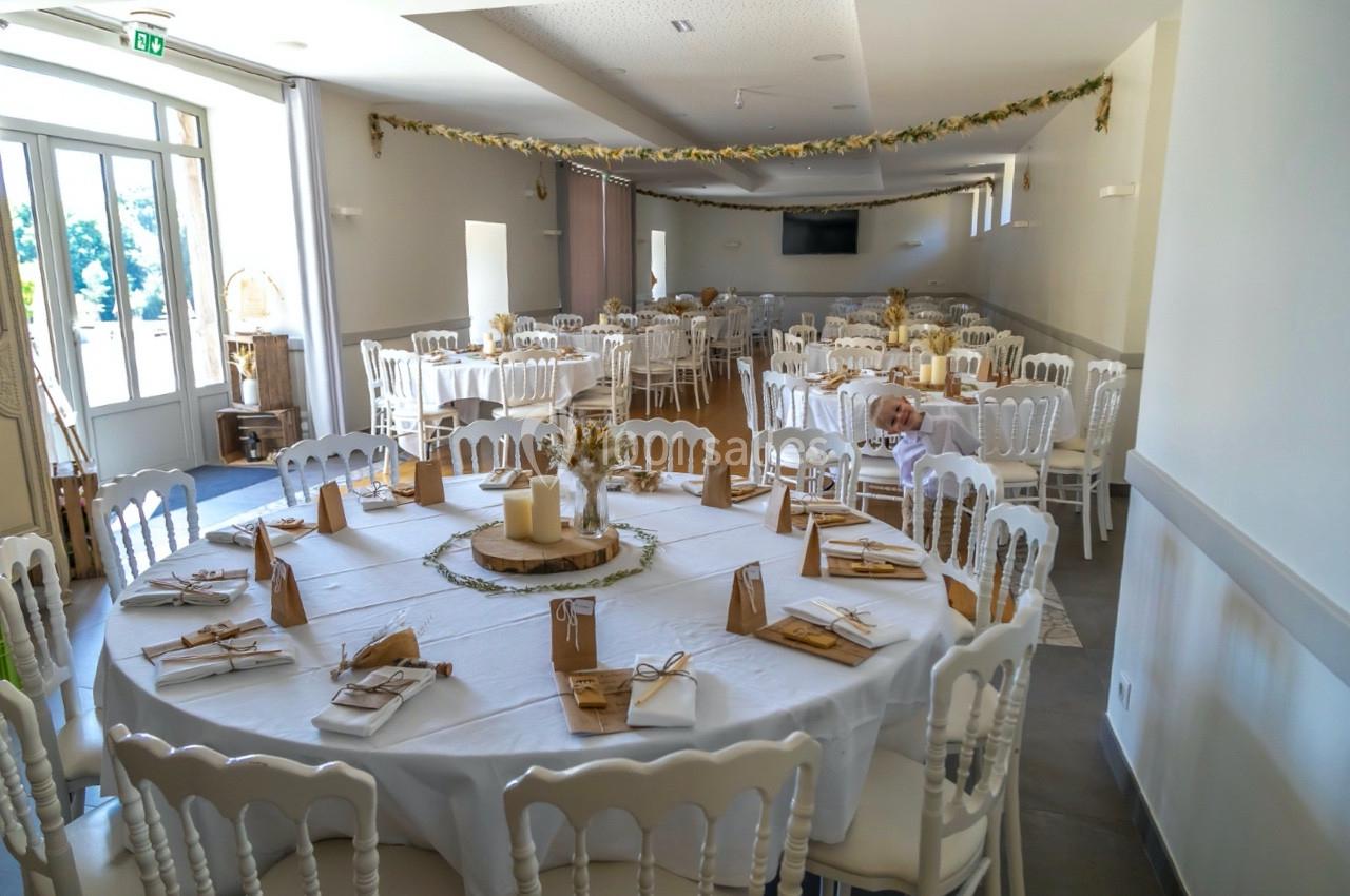 Salle de réception décorée avec des tables rondes dressées, ornées de bougies et d'éléments naturels.