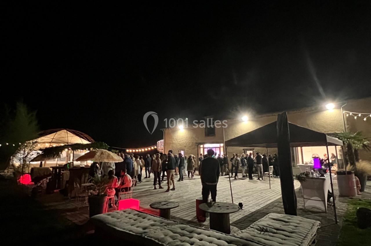 Groupe de personnes rassemblées de nuit sur une terrasse éclairée, avec des guirlandes lumineuses et des espaces aménagés.