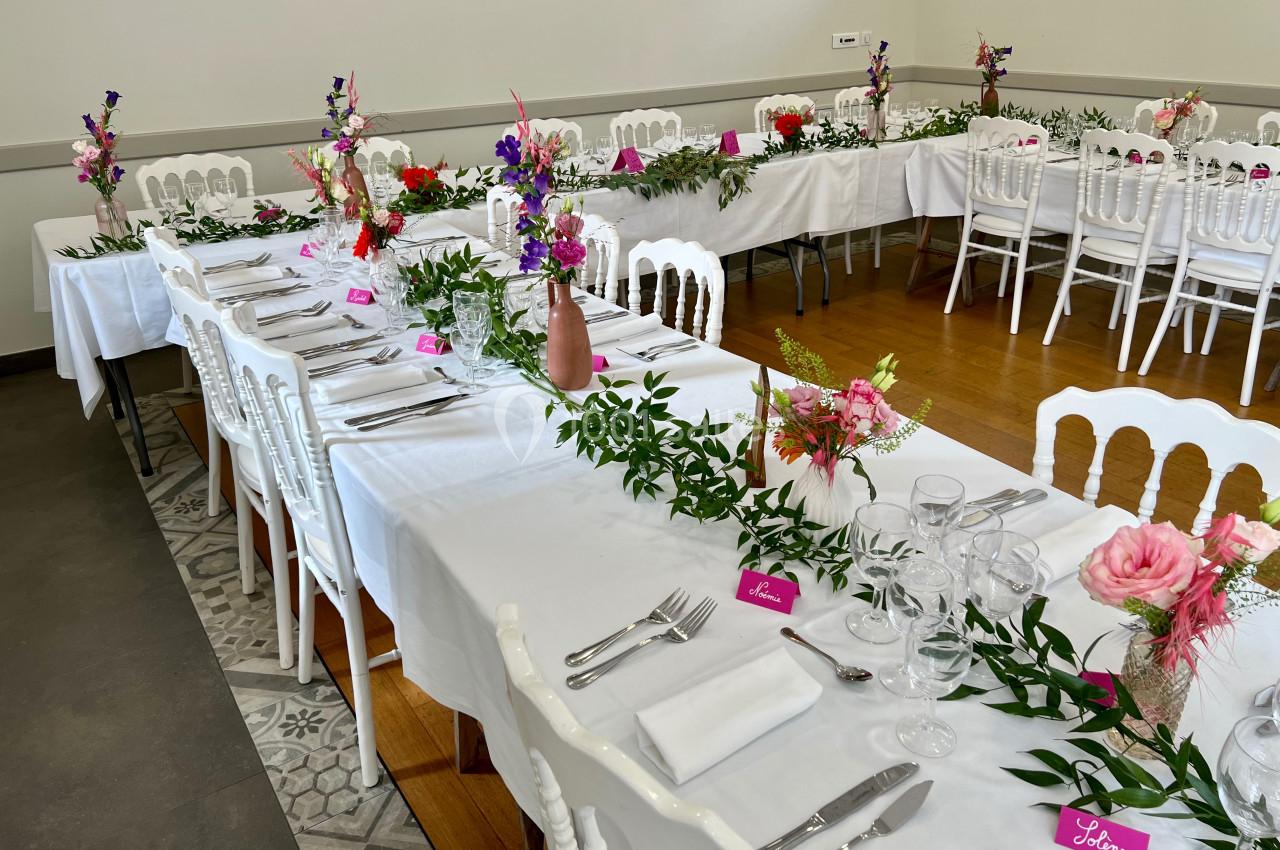 Tables décorées pour un événement avec nappes blanches, fleurs colorées, vaisselle et marque-places roses.