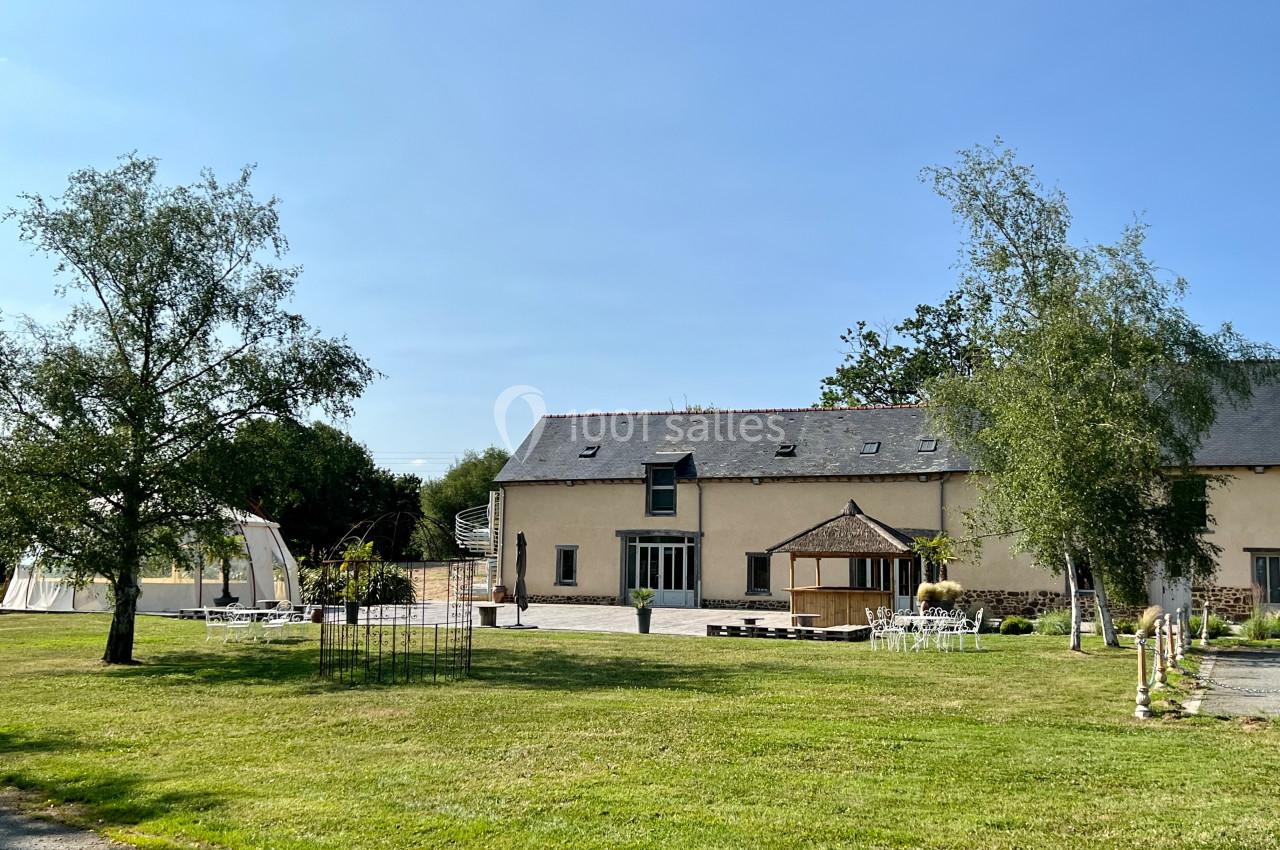 Bâtiment en pierre rénové avec toit en ardoise, entouré d'un jardin verdoyant et d'une terrasse aménagée.