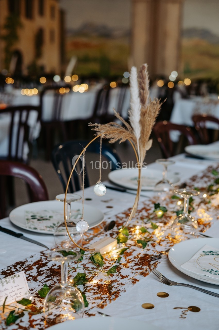 Centre de table décoratif avec pampas, guirlandes lumineuses et éléments naturels sur une nappe blanche.