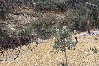 Table de pique-nique en bois sur un sol de gravier, entourée d'arbres dans un cadre naturel.