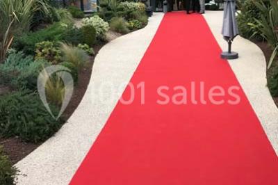 Tente blanche avec mobilier de jardin noir sur tapis rouge, installée devant une entrée vitrée d'un bâtiment beige.