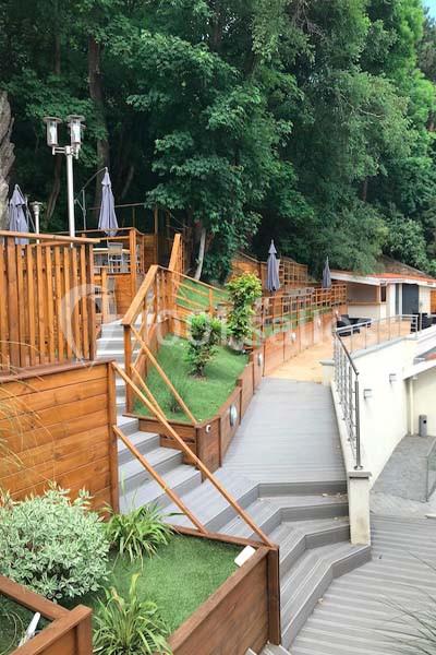 Escalier en bois et terrasse aménagée avec végétation, bordant une zone boisée et des parasols fermés.