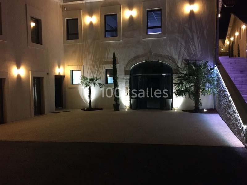 Façade d'un bâtiment éclairé de nuit avec des palmiers et une entrée voûtée en pierre.