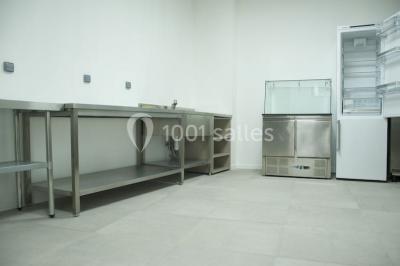 Miniature Location salle Lyon 9 (Rhône) - Hub de l'Ile Barbe #27 Cuisine professionnelle vide avec plans de travail en inox, évier, étagères ouvertes et réfrigérateurs en arrière-plan.