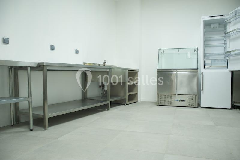 Location salle Lyon 9 (Rhône) - Hub de l'Ile Barbe #27 Cuisine professionnelle vide avec plans de travail en inox, évier, étagères ouvertes et réfrigérateurs en arrière-plan.