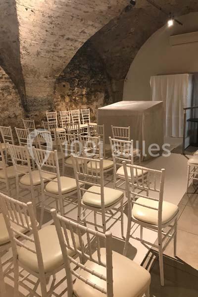 Location salle Lyon 9 (Rhône) - Hub de l'Ile Barbe #11 Chaises blanches disposées en rangées dans une salle voûtée en pierre avec une estrade couverte à l'avant.