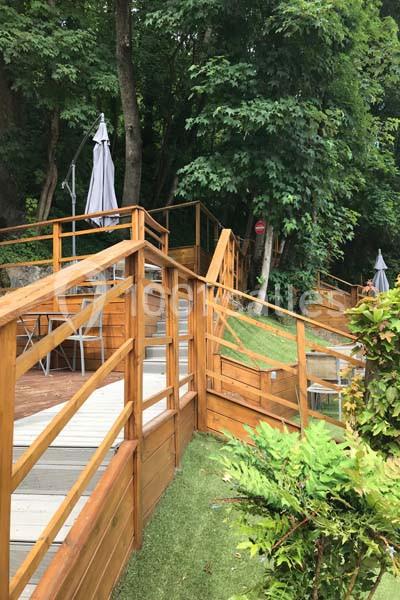 Location salle Lyon 9 (Rhône) - Hub de l'Ile Barbe #17 Terrasse en bois avec escaliers et rampes, entourée de végétation dense et de parasols fermés.