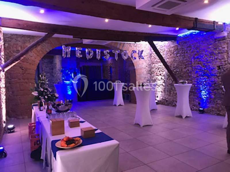 Location salle Lyon 9 (Rhône) - Hub de l'Ile Barbe #19 Salle de réception décorée avec des lumières bleues, des tables hautes et un buffet, dans un cadre en pierre apparente.