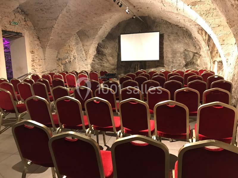 Location salle Lyon 9 (Rhône) - Hub de l'Ile Barbe #8 Salle voûtée en pierre avec des rangées de chaises rouges disposées face à un écran de projection blanc.
