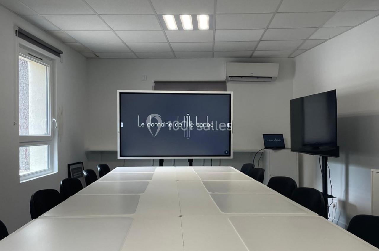 Location salle Lyon 9 (Rhône) - Hub de l'Ile Barbe #2 Salle de réunion lumineuse avec une grande table blanche, un écran interactif affichant ’Le domaine de l'île barbe’ et un…