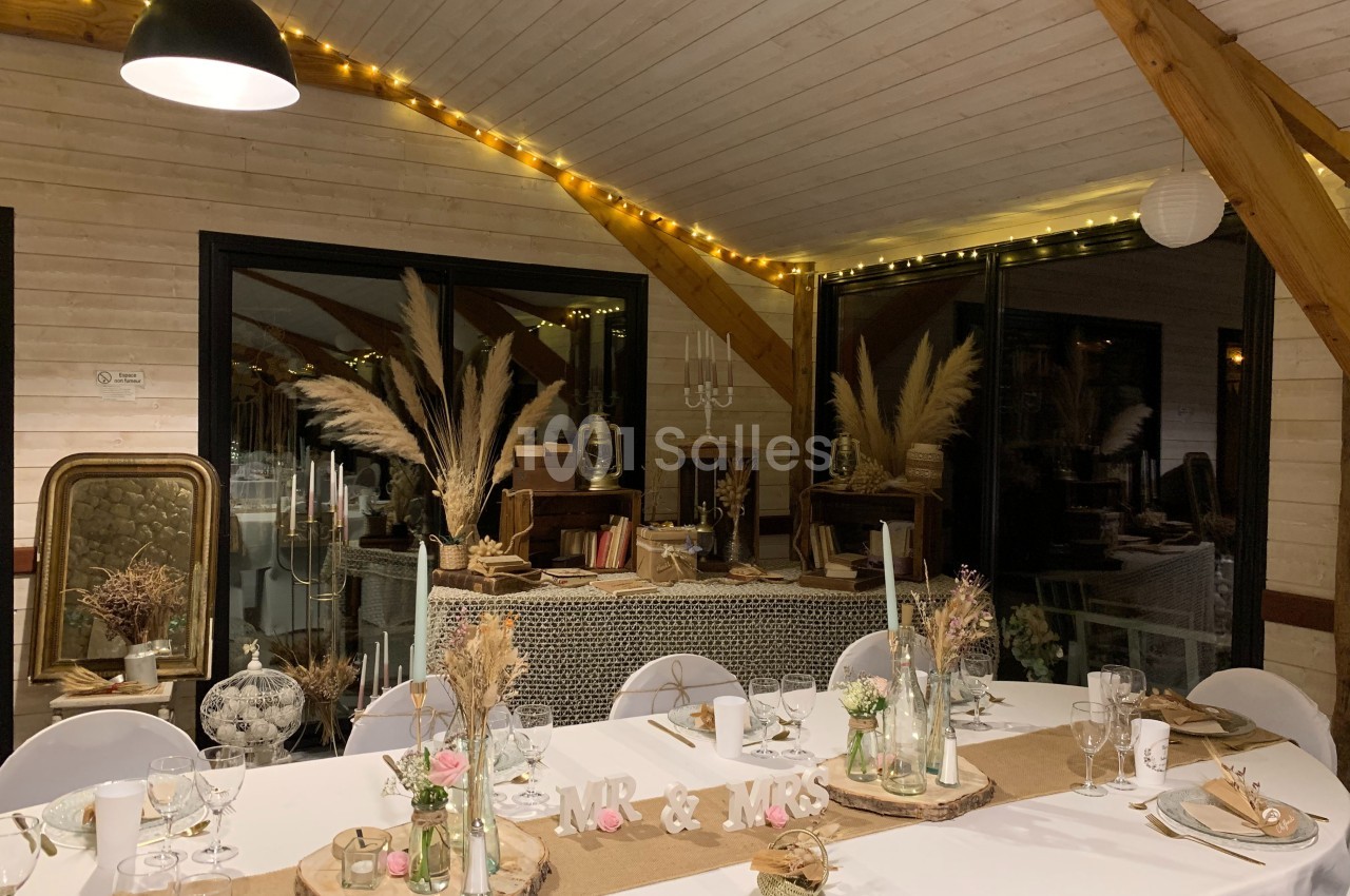 Salle décorée pour un mariage avec table dressée, pampas, guirlandes lumineuses et éléments rustiques.