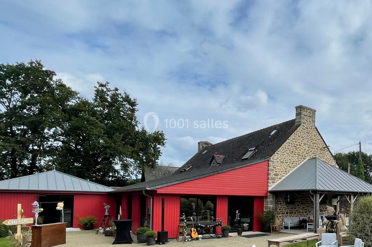 Bâtiment en pierre avec extensions rouges, entouré de mobilier extérieur blanc et d'arbres sous un ciel nuageux.