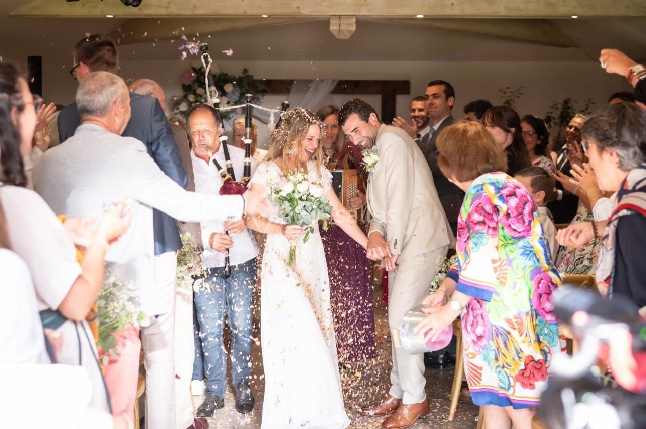 Un couple de mariés souriants sort sous une pluie de confettis, entouré d'invités applaudissant dans une salle festive.